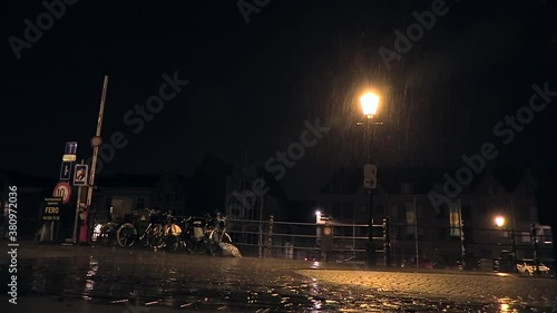 car passing over a bridge when lightning strikes with pouring rain at night in the city of Mechelen, Belgium photo