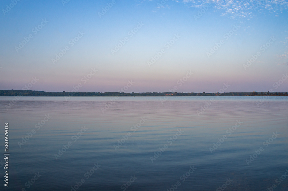 Sunrise over blue big lake with sky reflection in water