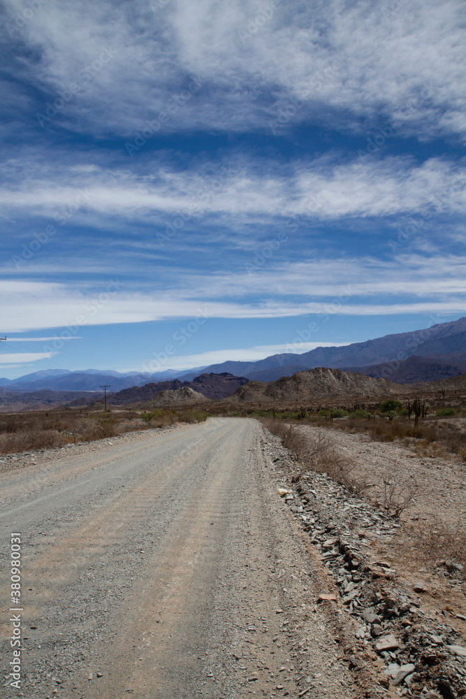 Desert route across the death valley. View of the dirt road, desert and mountains under a beautiful blue sky with clouds. Desert route across the death valley. View of the dirt road, desert and mountains under a beautiful blue sky with clouds.