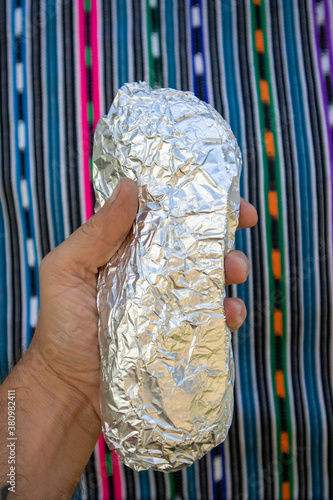 Photography Large Whole California-style Burrito Wrapped in Foil being held in a Hand