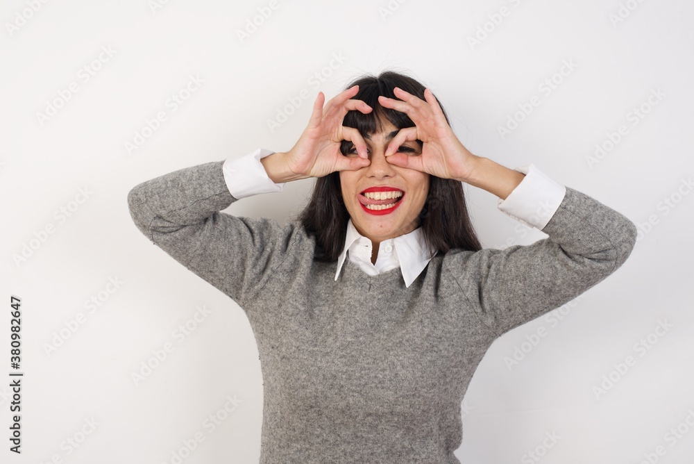 Young businesswoman with retro short hair wearing casual clothes standing over isolated white doing ok gesture like binoculars sticking tongue out, eyes looking through fingers. Crazy expression. Young businesswoman with retro short hair wearing casual clothes standing over isolated white doing ok gesture like binoculars sticking tongue out, eyes looking through fingers. Crazy expression.
