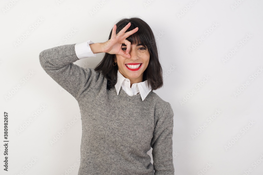 Young businesswoman with retro short hair wearing casual clothes standing over isolated white background doing ok gesture with hand smiling, eye looking through fingers with happy face. Young businesswoman with retro short hair wearing casual clothes standing over isolated white background doing ok gesture with hand smiling, eye looking through fingers with happy face.