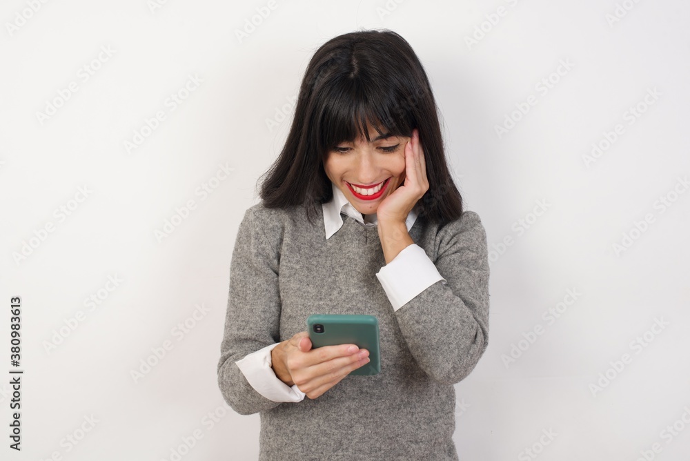Young businesswoman with retro short hairdo wearing casual clothes standing over isolated white background holding in hands cell reading sms using new app 5g Young businesswoman with retro short hairdo wearing casual clothes standing over isolated white background holding in hands cell reading sms using new app 5g