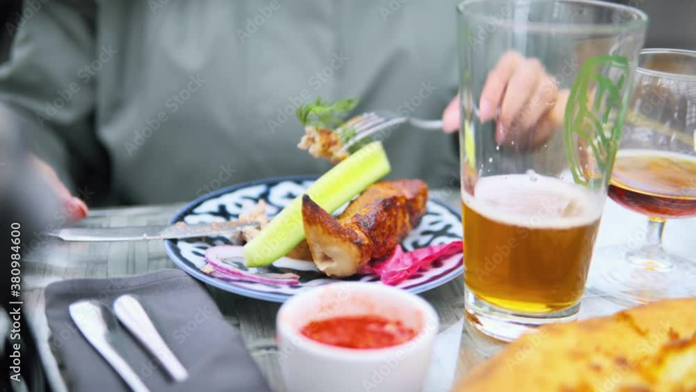 A woman puts a piece of cucumber on a plate where she has a piece of meat or chicken. On the plate there are greens, pink cabbage and potatoes. Next to the table there is a glass of beer and a glass A woman puts a piece of cucumber on a plate where she has a piece of meat or chicken. On the plate there are greens, pink cabbage and potatoes. Next to the table there is a glass of beer and a glass