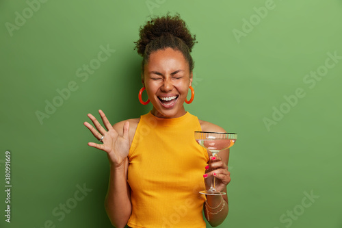 Valokuva Horizontal shot of overjoyed emotional Afro American curly woman laughs happily