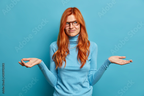 Photography Photo of indifferent good looking woman with long red hair spreads palms and loo