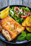 Fish dish - fried cod fillet with potatoes and vegetable salad on wooden table
