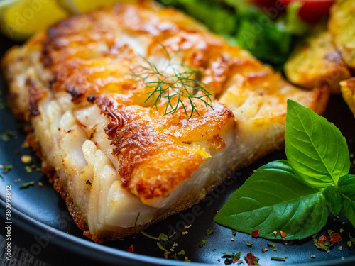 Fotografie Fish dish - fried cod fillet with potatoes and vegetable salad on wooden table
