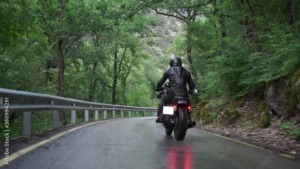 Motorcyclist riding slow on country road on a mountainous southern road serpentine. Footage. Two strong young pilots in helmets drive along a winding wet road in the forest. Adventure lifestyle. Motorcyclist riding slow on country road on a mountainous southern road serpentine. Footage. Two strong young pilots in helmets drive along a winding wet road in the forest. Adventure lifestyle.