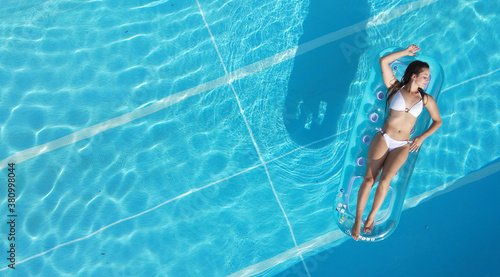 Sexy girl enjoys the sun in the crystal clear water of a swimming pool - view from above