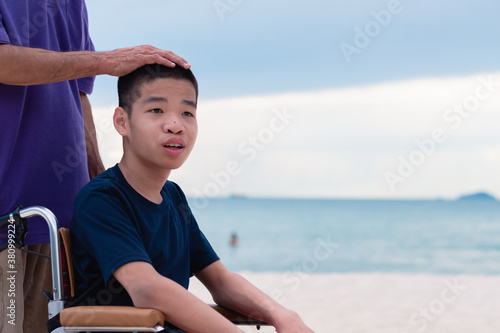 Asian special child on wheelchair is smiling, playing and doing activity on the sea beach, Lifestyle of disability child, Life in the education age, Happy disabled kid in travel holidays concept. © GAYSORN