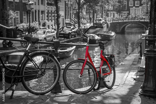 A picture of a red bike on the bridge over the channel in Amsterdam. The background is black and white. 
