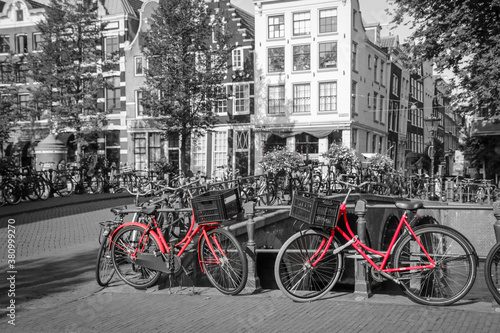 A picture of two red bikes on the bridge over the channel in Amsterdam. The background is black and white. 