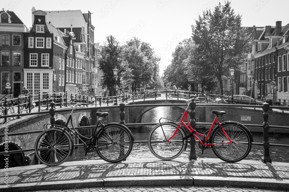 A picture of a red bike on the bridge over the channel in Amsterdam. The background is black and white. 