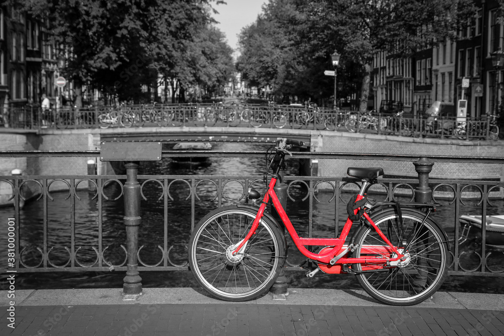 A picture of a red bike on the bridge over the channel in Amsterdam. The background is black and white. 