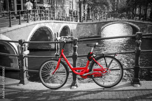 A picture of a red bike on the bridge over the channel in Amsterdam. The background is black and white. 