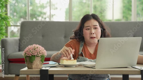 Asian plus size woman in casual eating working online with laptop computer online at home, eating unhygienic food
 photo