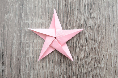 Pink origami paper star on wooden background