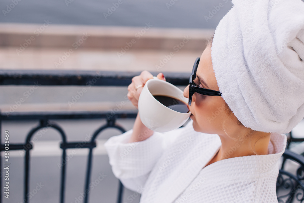 Stylish young girl blogger in white robe, towel and sunglasses on balcony drinking milk or coffee. Lazy morning Stylish young girl blogger in white robe, towel and sunglasses on balcony drinking milk or coffee. Lazy morning