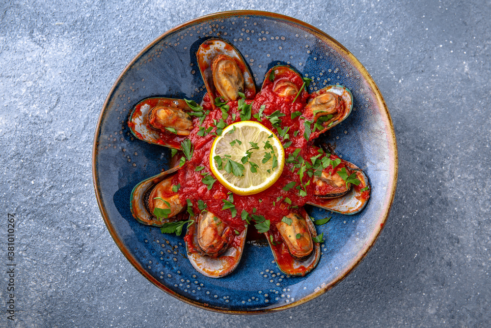 Mussels in a spicy tomato sauce. Natural delicious food. Greek cuisine menu. Still life in a marine style on a blue background. Mussels in a spicy tomato sauce. Natural delicious food. Greek cuisine menu. Still life in a marine style on a blue background.