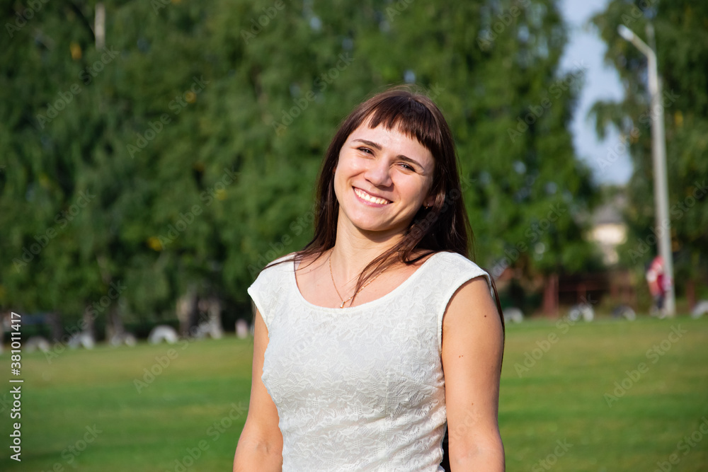 Young beautiful Caucasian girl in a short white dress with long hair on a green background of a football field and the sky at the stadium. Front view. Young beautiful Caucasian girl in a short white dress with long hair on a green background of a football field and the sky at the stadium. Front view.