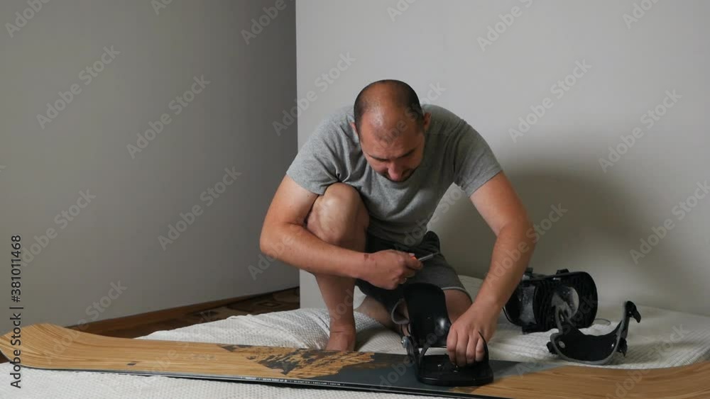 A man attaches bindings to a snowboard at home. Prepares the snowboard for winter A man attaches bindings to a snowboard at home. Prepares the snowboard for winter
