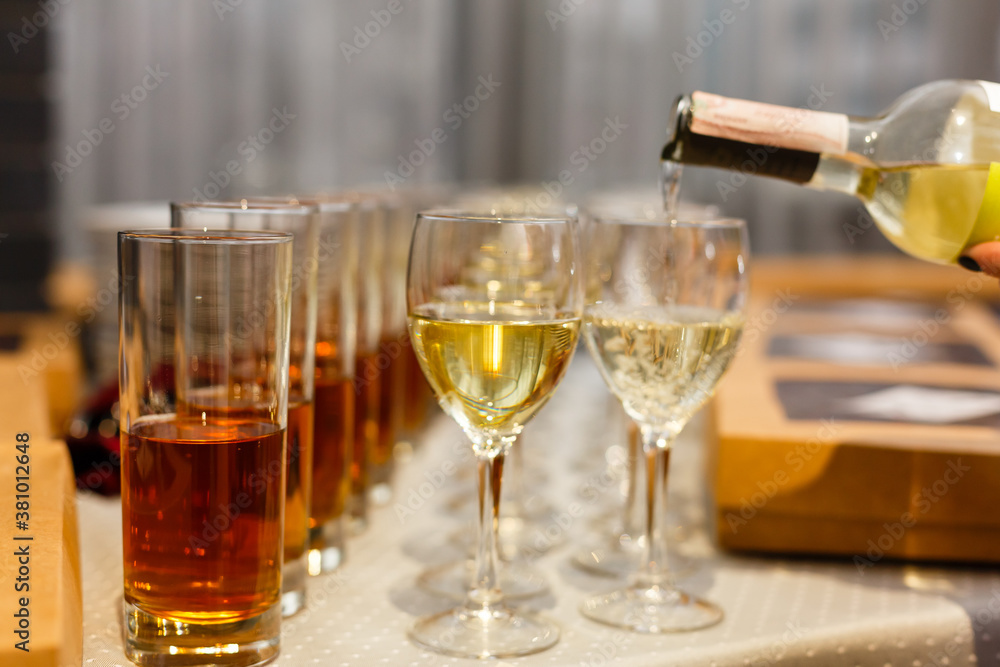 White wine being poured into wine glass in restaurant. Set of glasses with juice