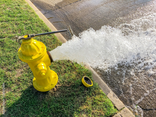 Top view yellow fire hydrant gushing water across a residential street near Dallas, Texas, USA photo