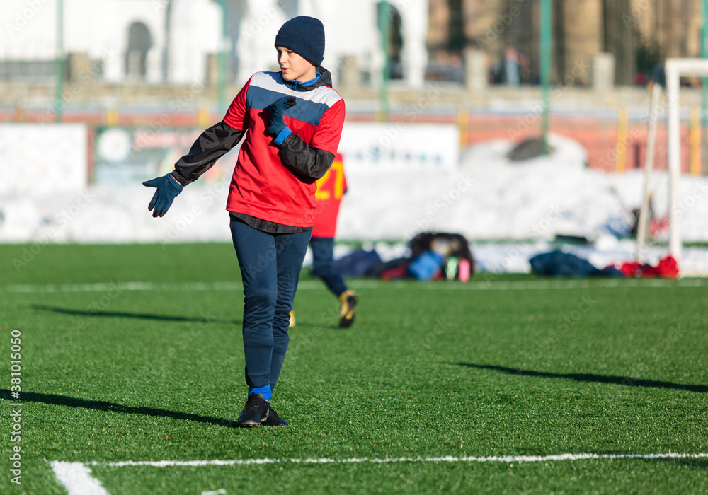 Obraz premium Boys in red sportswear running on soccer field with snow on background. Young footballers dribble and kick football ball in game. Training, active lifestyle, sport, children winter activity