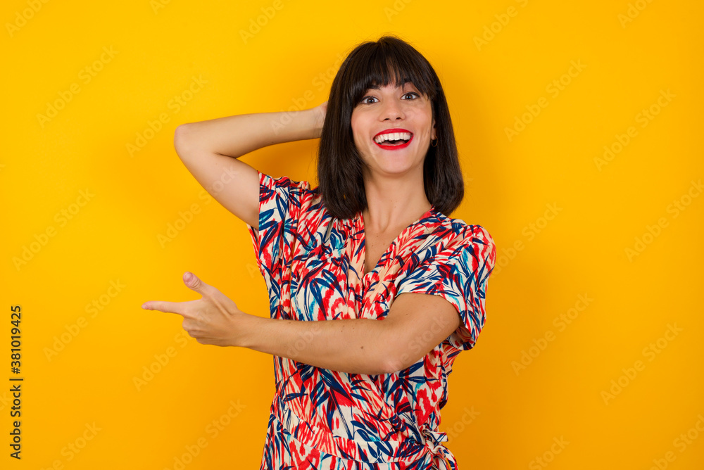 Positive glad female says: wow how exciting it is, has amazed expression, indicates something. Joyful pretty young woman demonstrates something. One hand on her head and pointing with other hand. Positive glad female says: wow how exciting it is, has amazed expression, indicates something. Joyful pretty young woman demonstrates something. One hand on her head and pointing with other hand.