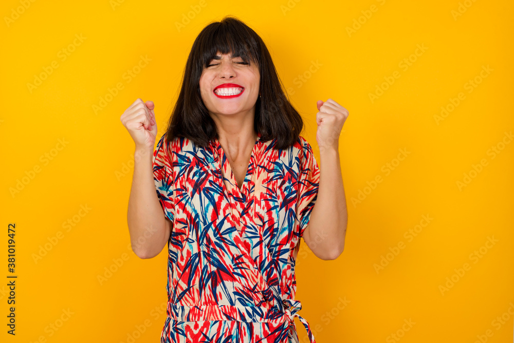 Caucasian brunette woman rejoicing her success and victory clenching her fists with joy. Lucky woman being happy to achieve her aim and goals. Positive emotions, feelings. Caucasian brunette woman rejoicing her success and victory clenching her fists with joy. Lucky woman being happy to achieve her aim and goals. Positive emotions, feelings.