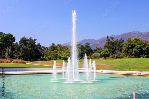 a gorgeous summer landscape at the LA Arboretum with a water fountain, lush green trees, plants and grass, mountains and blue sky in Arcadia California USA photo