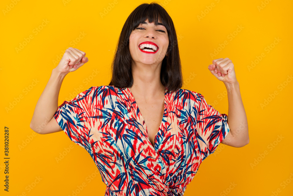 Waist up portrait of strong successful determined young female winner in casual t-shirt raising arms, clenching fists, exclaiming with joy and excitement. Victory, success and achievement concept. Waist up portrait of strong successful determined young female winner in casual t-shirt raising arms, clenching fists, exclaiming with joy and excitement. Victory, success and achievement concept.