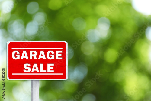 Sign with phrase GARAGE SALE on blurred green background, bokeh effect