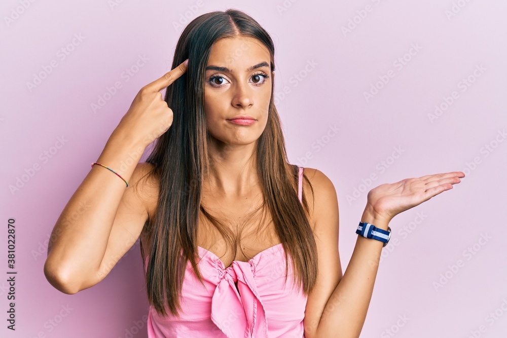 Young hispanic woman wearing casual style with sleeveless shirt confused and annoyed with open palm showing copy space and pointing finger to forehead. think about it. Young hispanic woman wearing casual style with sleeveless shirt confused and annoyed with open palm showing copy space and pointing finger to forehead. think about it.