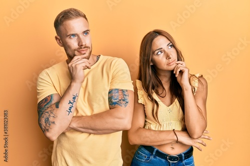 Young couple of girlfriend and boyfriend hugging and standing together with hand on chin thinking about question, pensive expression. smiling with thoughtful face. doubt concept.