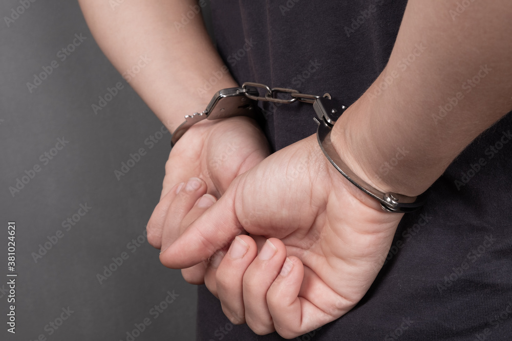 arrested person in handcuffs on a dark background close-up, chained hands on the back arrested person in handcuffs on a dark background close-up, chained hands on the back