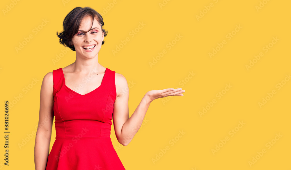 Beautiful young woman with short hair wearing casual style with sleeveless shirt smiling cheerful presenting and pointing with palm of hand looking at the camera. Beautiful young woman with short hair wearing casual style with sleeveless shirt smiling cheerful presenting and pointing with palm of hand looking at the camera.