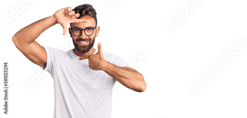 Young hispanic man wearing casual clothes and glasses smiling making frame with hands and fingers with happy face. creativity and photography concept.