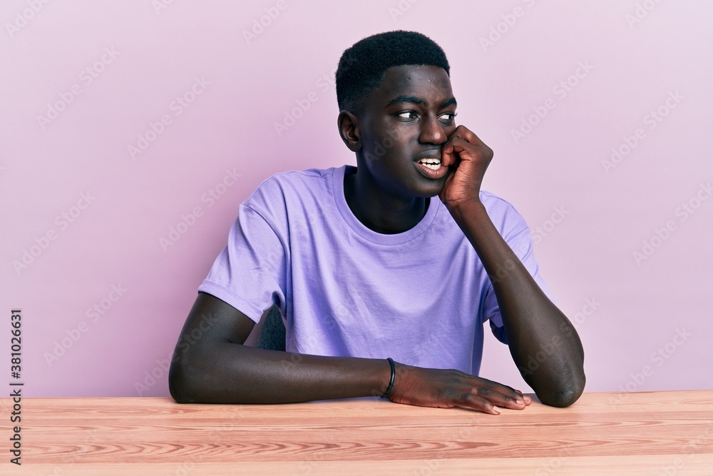 Young african american man wearing casual clothes sitting on the table looking stressed and nervous with hands on mouth biting nails. anxiety problem. Young african american man wearing casual clothes sitting on the table looking stressed and nervous with hands on mouth biting nails. anxiety problem.