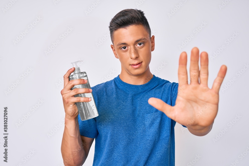 Young hispanic boy using hand sanitizer gel with open hand doing stop sign with serious and confident expression, defense gesture Young hispanic boy using hand sanitizer gel with open hand doing stop sign with serious and confident expression, defense gesture