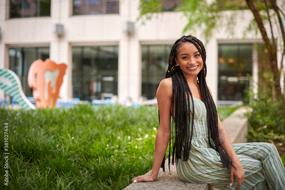 Fototapeta premium Stunning young biracial woman stands on city street in summer - wearing green striped romper