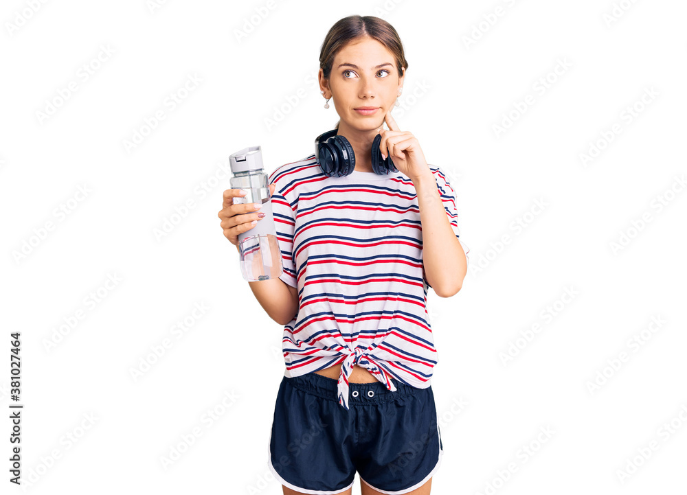 Beautiful caucasian woman with blonde hair wearing sportswear and headphones drinking a bottle of water serious face thinking about question with hand on chin, thoughtful about confusing idea Beautiful caucasian woman with blonde hair wearing sportswear and headphones drinking a bottle of water serious face thinking about question with hand on chin, thoughtful about confusing idea