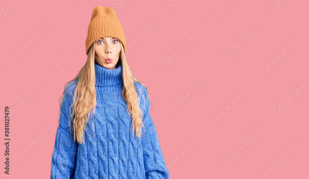 Beautiful caucasian woman with blonde hair wearing wool sweater and winter hat scared and amazed with open mouth for surprise, disbelief face Beautiful caucasian woman with blonde hair wearing wool sweater and winter hat scared and amazed with open mouth for surprise, disbelief face