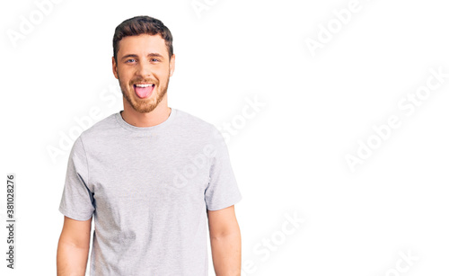 Handsome young man with bear wearing casual tshirt sticking tongue out happy with funny expression. emotion concept.