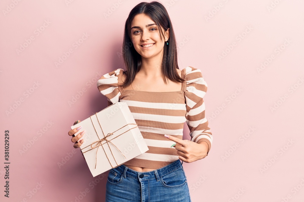 Young beautiful girl holding gift smiling happy pointing with hand and finger Young beautiful girl holding gift smiling happy pointing with hand and finger