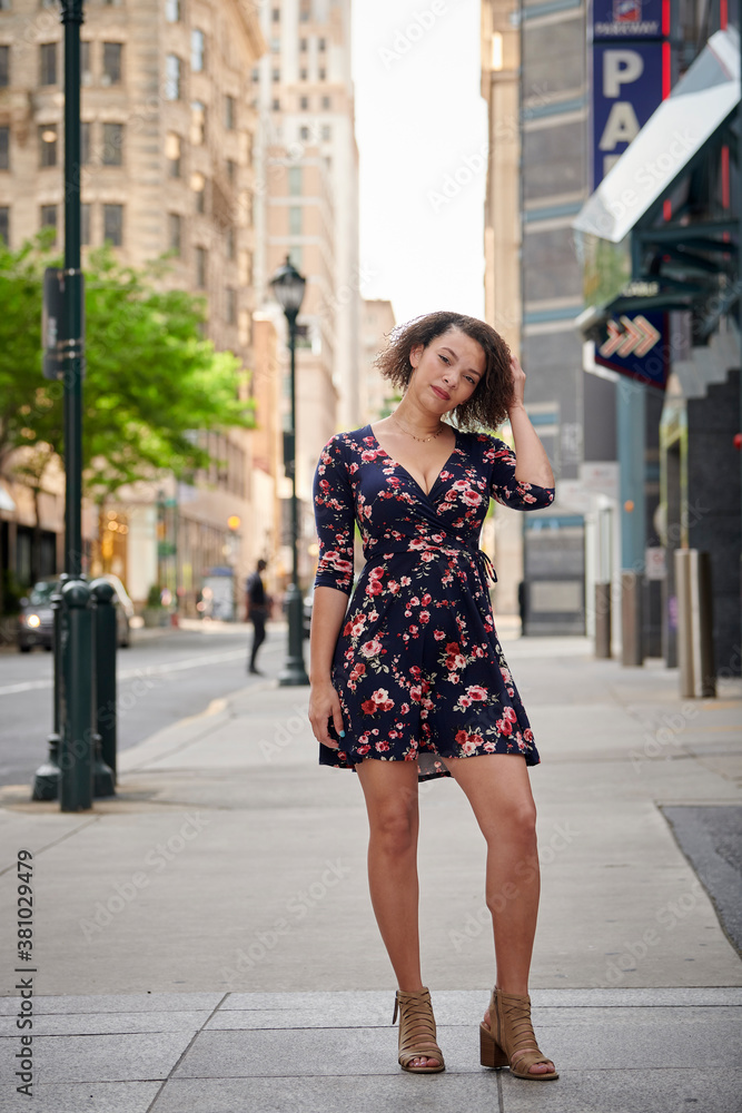 Beautiful biracial woman in floral print dress poses on sidewalk in downtown area