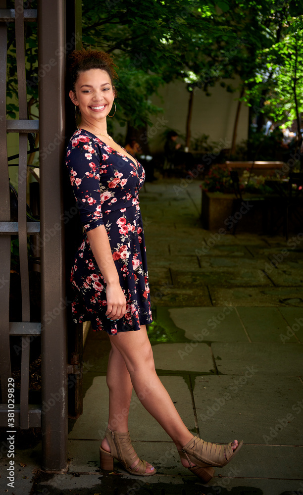 Naklejka premium Beautiful biracial woman in floral print dress poses in shaded city park - hair up