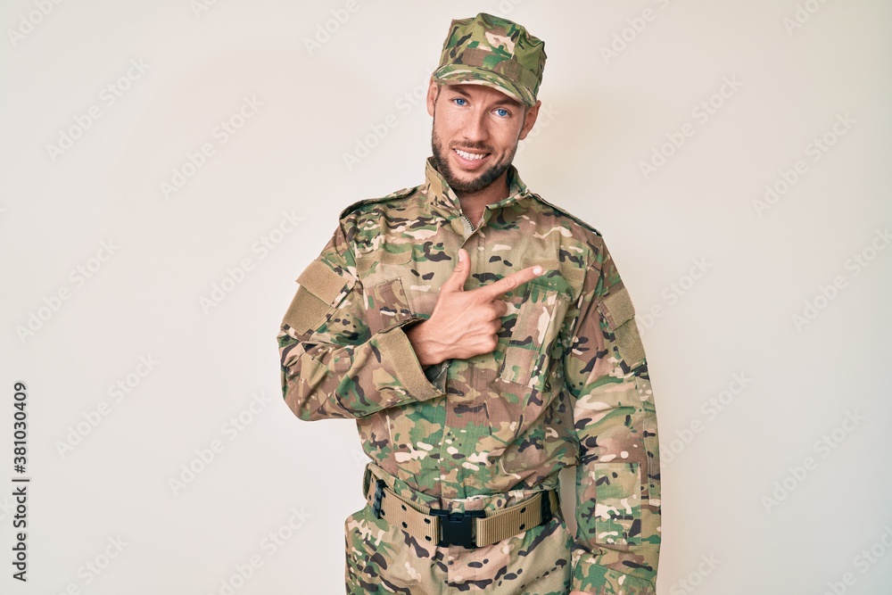 Young caucasian man wearing camouflage army uniform cheerful with a smile on face pointing with hand and finger up to the side with happy and natural expression Young caucasian man wearing camouflage army uniform cheerful with a smile on face pointing with hand and finger up to the side with happy and natural expression