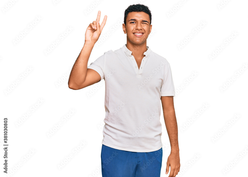 Young arab man wearing casual clothes smiling with happy face winking at the camera doing victory sign with fingers. number two. Young arab man wearing casual clothes smiling with happy face winking at the camera doing victory sign with fingers. number two.